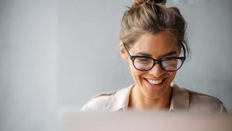 Nainen hymyilee tietokoneelleen