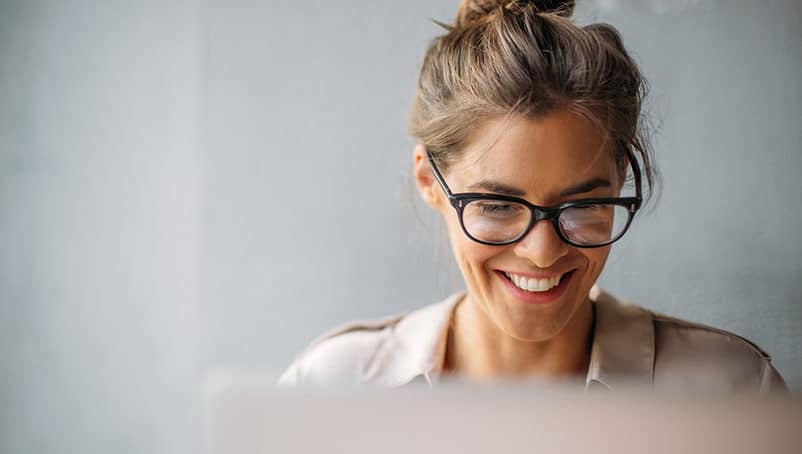 Nainen hymyilee tietokoneelleen